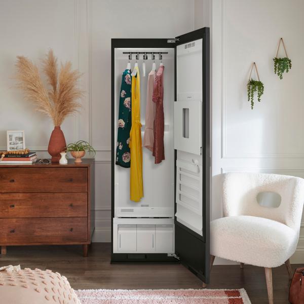 The LG Styler® Smart Steam Closet in a nicely decorated bedroom with the door open and displaying clothes hanging in it.