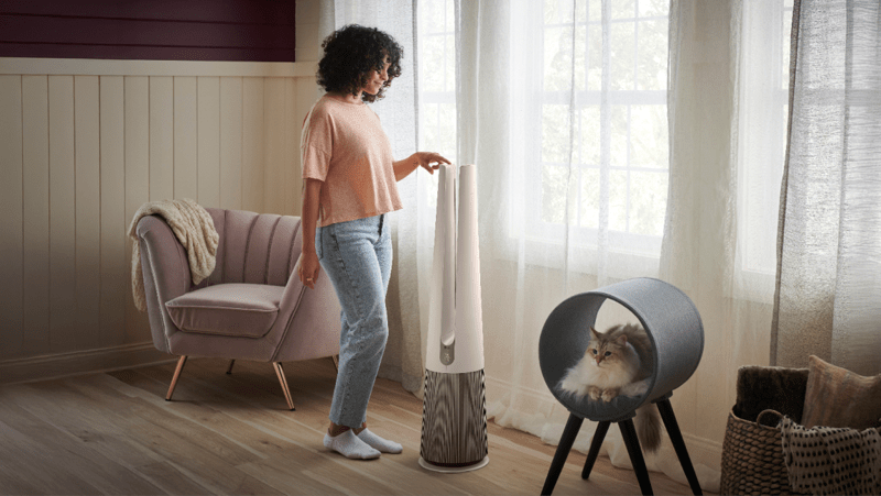 A woman adjusts her PuriCare™ air purifier in a sun-filled room. 