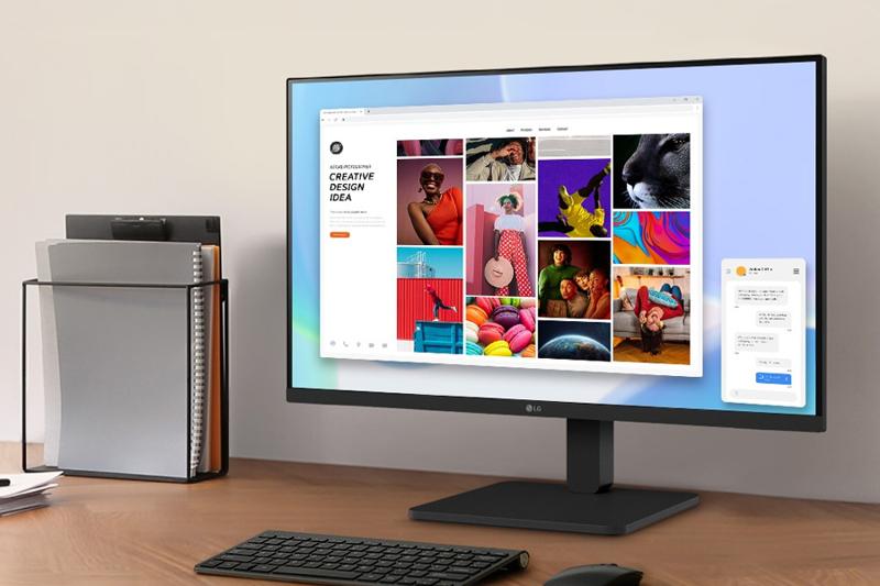 A computer monitor displaying a colorful webpage with a keyboard and file holder on a wooden desk.