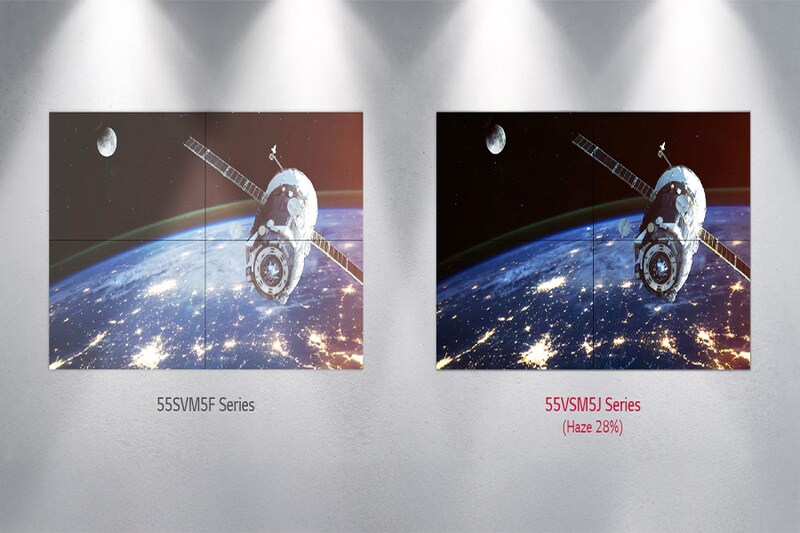 The image shows two large digital displays mounted on a wall, each featuring an identical image of a satellite orbiting Earth. The displays are set in a brightly lit room, with focused spotlights illuminating the wall. The scene depicted on the screens includes a satellite with prominent solar panels against a backdrop of Earth's curvature, lit by city lights against the dark expanse of space. The moon is visible in the top left corner of both images. The left display has the label "55SVM5F Series" beneath it, while the right display is labeled "55VSMSJ Series (Haze 28%)" in red text.