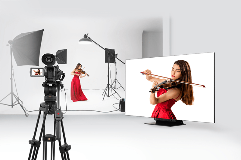 Violinist in red dress playing in a photography studio with camera and monitor.