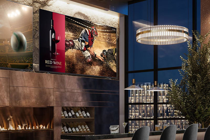 A bar area with screens displaying a baseball scene and red wine ad, under atmospheric lighting in a modern interior.