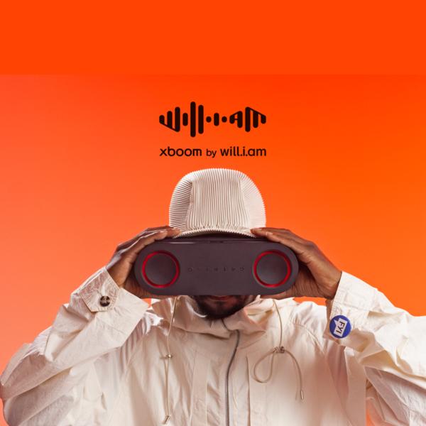 Artist will.i.am holds an xboom speaker on an orange background.