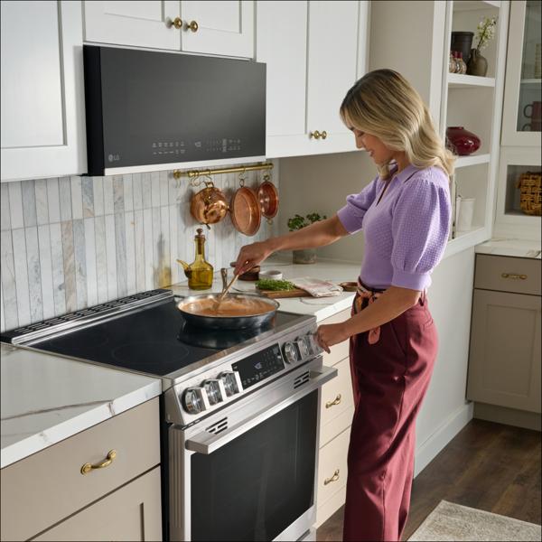 A woman cooking a dish on the LG Smart Induction Slide-in Range in a modern, white kitchen.