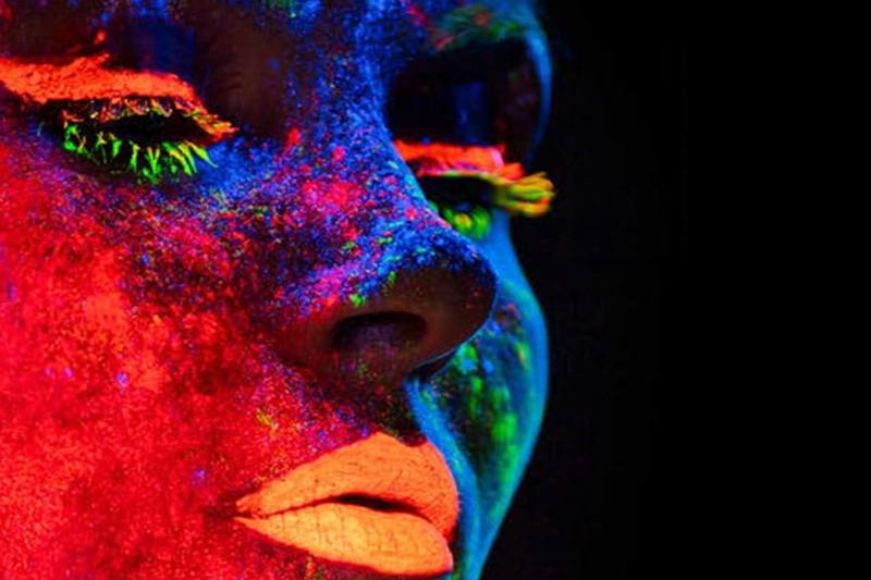 Close-up of a face with neon UV paint in vibrant colors against a black background.