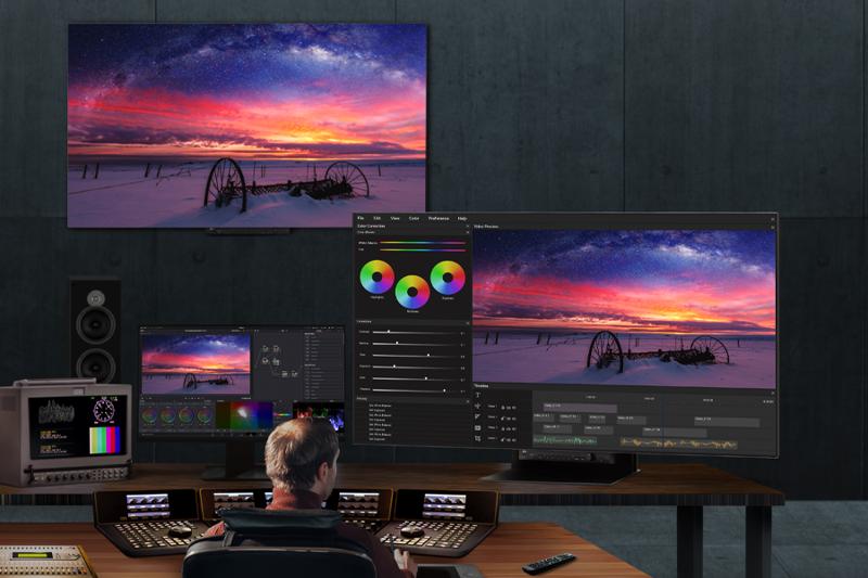 A video editing setup with multiple monitors displaying a sunset image, editing software, and professional audio and video equipment
