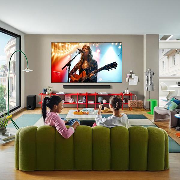 The LG 77 inch Class OLED evo AI C5 TV in a cozy living room two women watching a live concert on the screen.