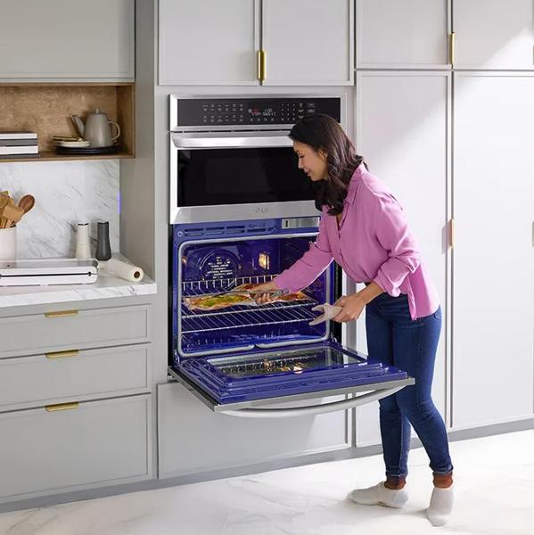 A woman in a bright white kitchen cooking food in the LG Smart Combination Wall Oven.