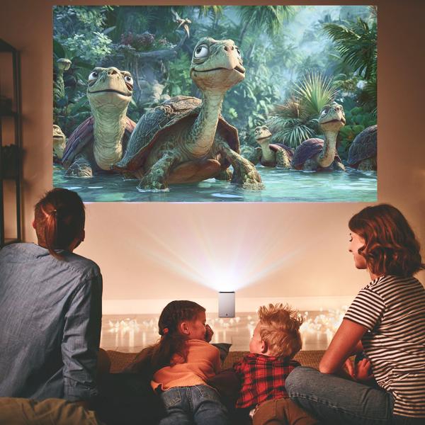 The LG CineBeam Q 4K Projector projecting an animated ocean scene with turtle characters on the wall of a modern living room with a family nestled on the floor together.
