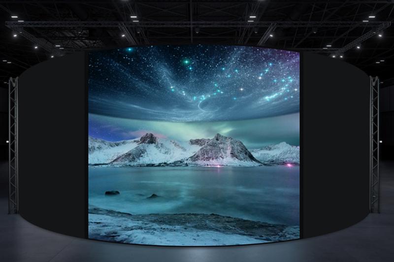 Curved digital display showing a snow-covered mountain landscape under a night sky with auroras and stars.