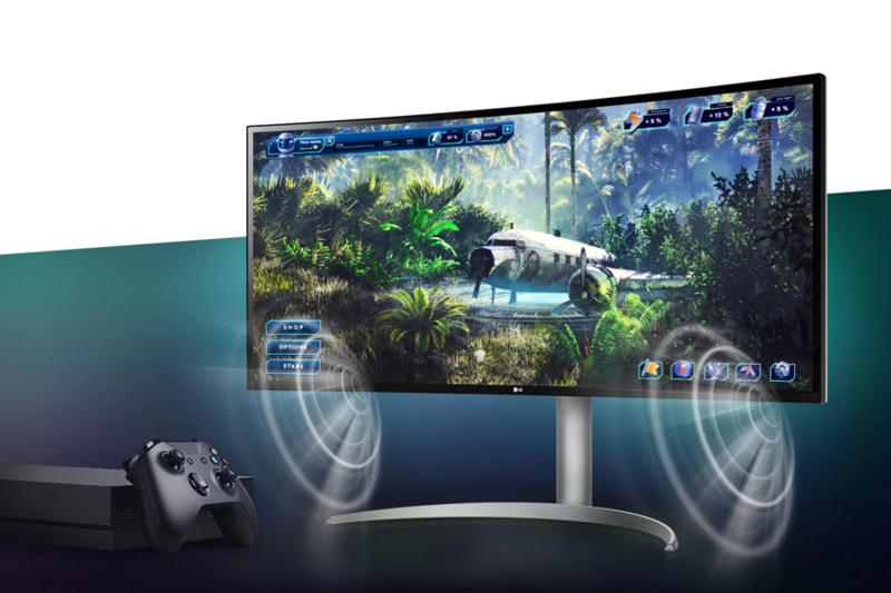 A curved monitor displays a jungle game scene with a plane wreck; a game console and controller are in the foreground.