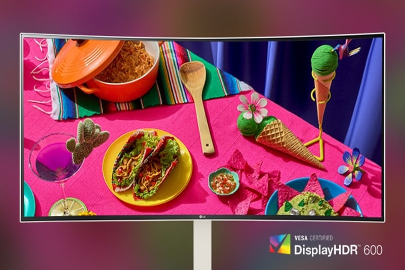 Vivid table setting with tacos, an orange pot, and decorative elements displayed on a curved monitor.