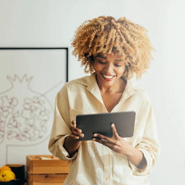 A woman smiles as she reads something on her tablet.