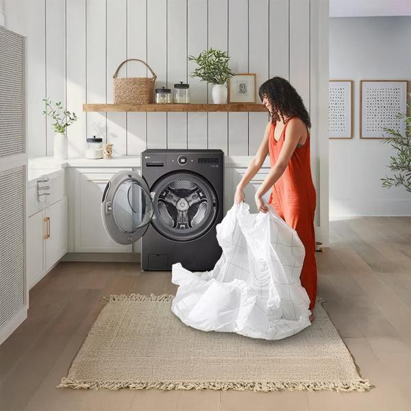 A woman taking her sheets out of the LG Ventless Washer Dryer Combo LG WashCombo™ in a white laundry cottage core room.