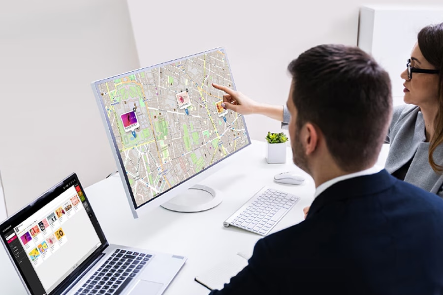 Two people discussing over a computer monitor showing a map.