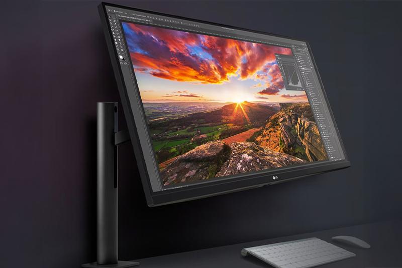 Black monitor displaying vibrant sunset landscape on a dark background with a keyboard and mouse below.