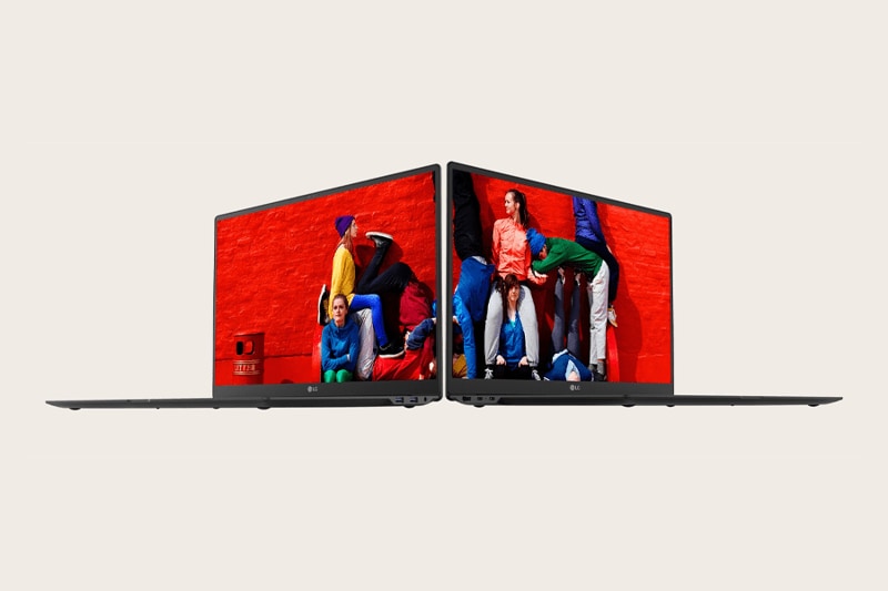 Two ultra-thin laptops back-to-back, displaying a colorful image of people in bright clothes against a red brick wall.