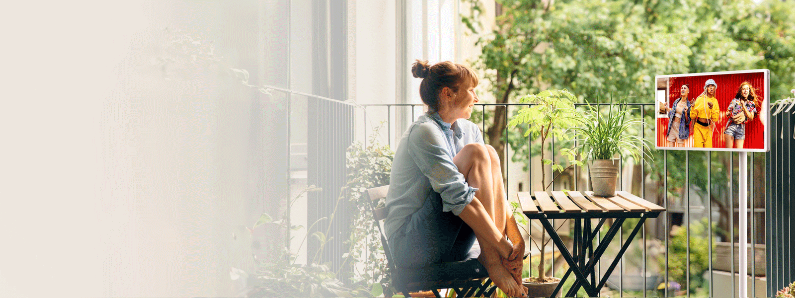 A woman watches content on a StanbyME 2 on her balcony. A detached StanbyME 2 screen lays flat on a surface while displaying a turntable interface. Front view of a StanbyME 2 home screen with various app icons surrounding it. 