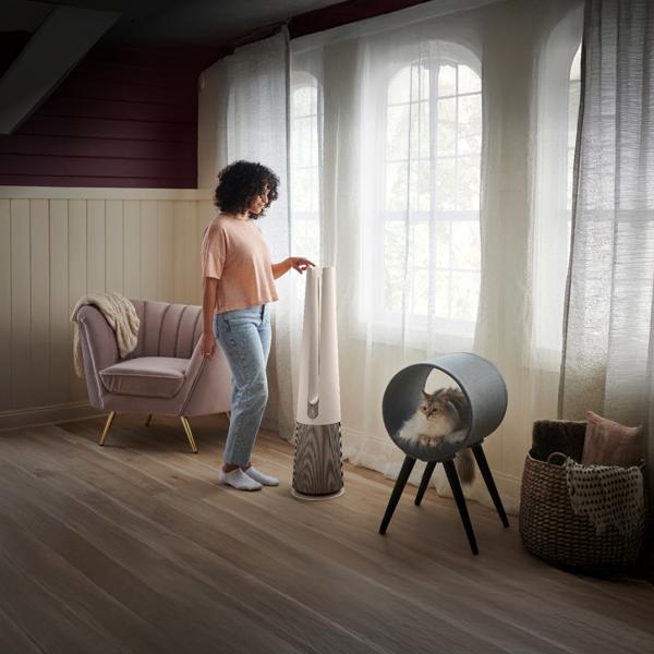 A woman adjusts her PuriCare™ air purifier in a sun-filled room. 