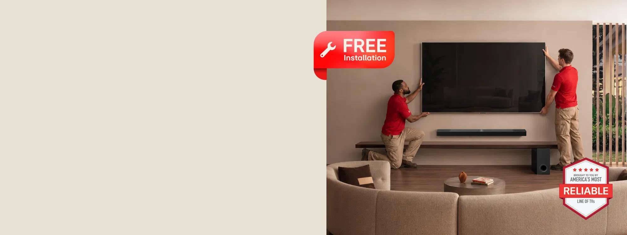 Two installers in red shirts mounting an LG TV on a wall in a living room, with a Soundbar and subwoofer on a shelf below. FREE Installation badge visible. Brought to you by America's Most Reliable Line of TVs badge visible.
