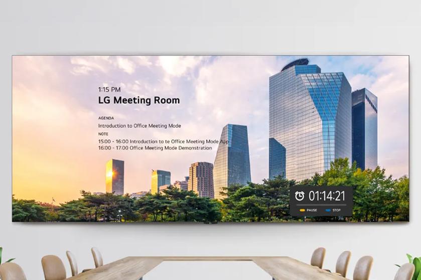 A digital screen in a meeting room showing a cityscape with skyscrapers, meeting agenda, and a timer.