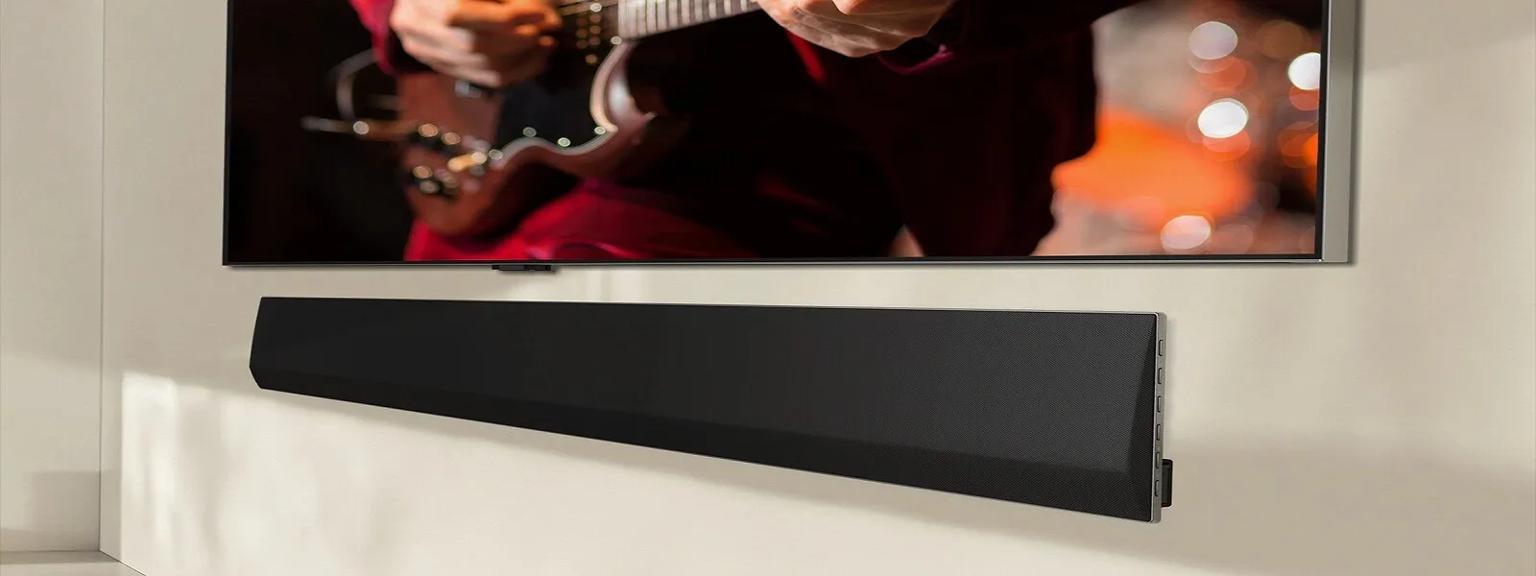 An LG Soundbar positioned below a TV screen shows a person playing an electric guitar. The focus is on their hands and the guitar, set against a warm, blurred background that creates a cozy atmosphere. This setup emphasizes a high-quality entertainment system.