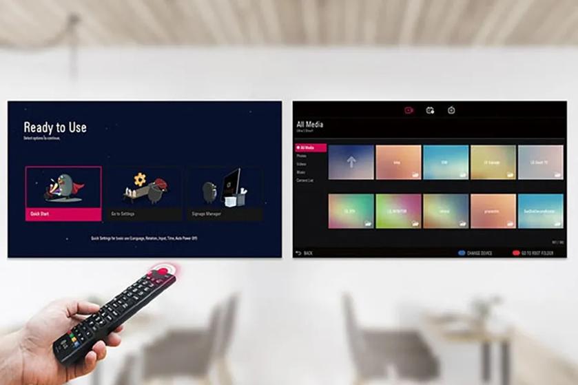 The image features two television screens side by side in a room with a blurred background. The screen on the left displays a "Ready to Use" interface with a dark blue background. It contains three graphic icons: "Quick Start," "Go to Settings," and "Signage Manager," each accompanied by a penguin-like character performing different activities. The screen on the right shows an "All Media" menu with a black background. It has two rows of colorful, gradient-tinted rectangles representing different media options such as "Photo," "Video," and "Music." In the foreground, a hand holds a black remote control with brightly colored buttons and a pink directional pad.