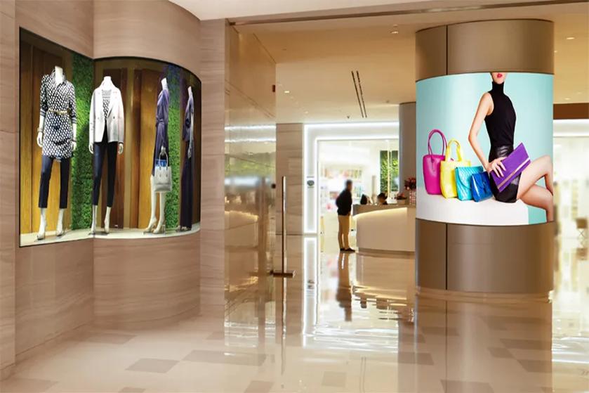 Retail interior with mannequin display and digital ad of a model with colorful handbags.