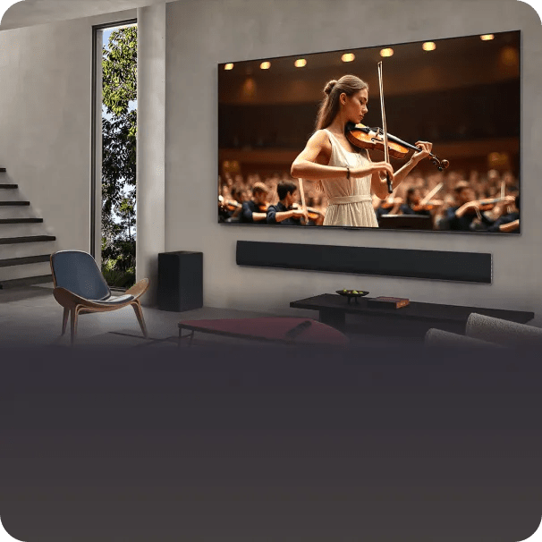 A modern living room with minimalist decor and natural light, featuring a large wall-mounted TV displaying a violinist performing on stage with an orchestra.