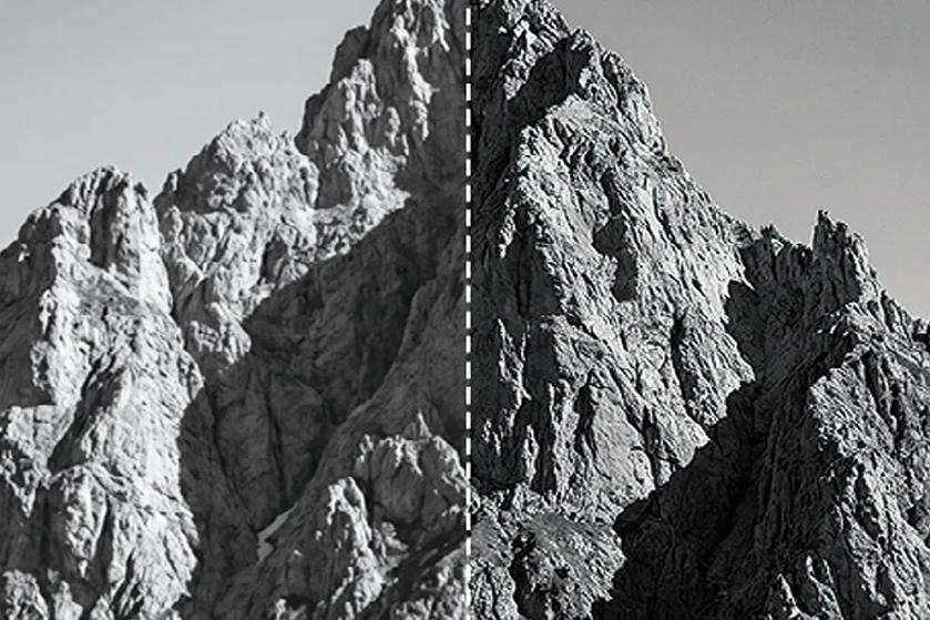 Grayscale split view of a jagged mountain range, divided by a vertical dashed white line, with lighter rock on the left and darker, higher-contrast rock on the right.