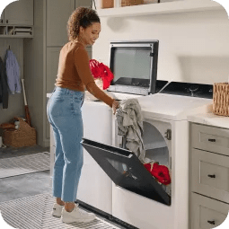A woman transfers wet clothing from a top load LG washer into a front load LG dryer.