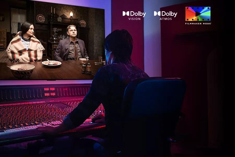 A man sits in front of a sound board watching a film on the LG OLED B4 with Dolby Vision™, Dolby Atmos® and FILMMAKER MODE™ logos.