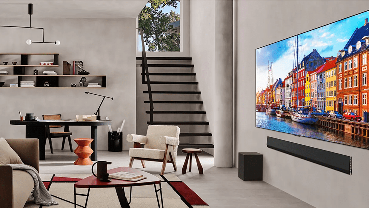 Modern living room with large TV showing a colorful cityscape, sleek soundbar, cozy seating, desk area, and open staircase.