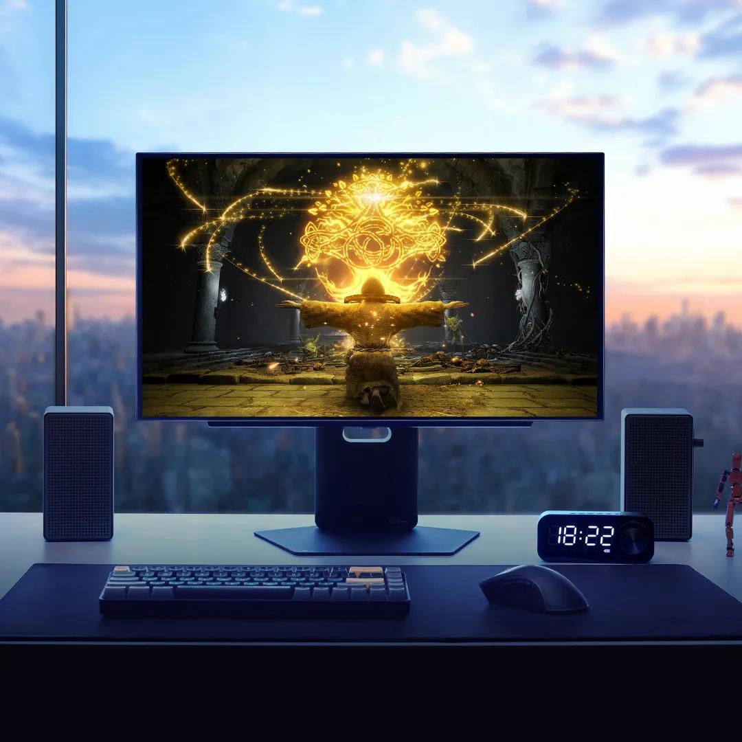 The LG 27 Inch UltraGear™ OLED Monitor with a video game on the screen sits on a desk with speakers, a mouse, keyboard and clock. A city skyline shows through the window in the background..