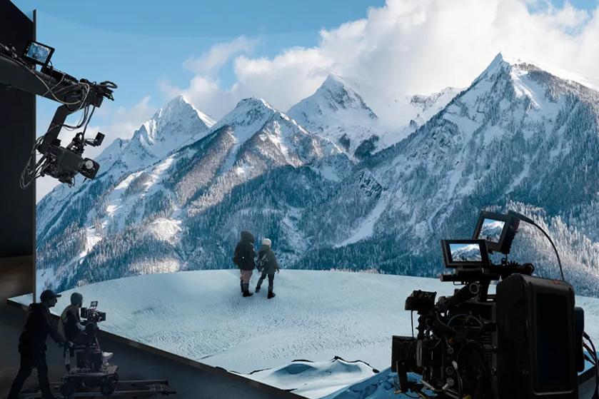 A pair of actors walk across a scene made with LG Studio Series as cameras roll. The displays feature a winter landscape full of mountains and snow.