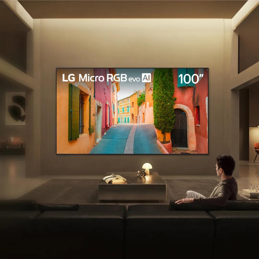 A man watches his Micro RGB TV from a couch in a stylish living room setting. “America’s Most Reliable Line of TVs” badge.