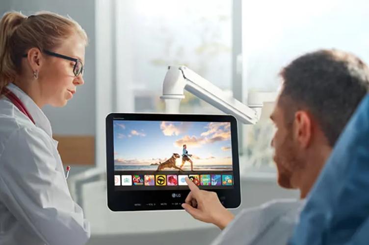 A patient reclining in a hospital bed uses an LG touch screen arm TV. 