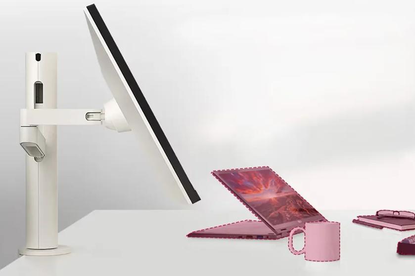 A desk with a white monitor arm holding a monitor, a pink open laptop, a pink mug, and pink notebooks with glasses on top. 