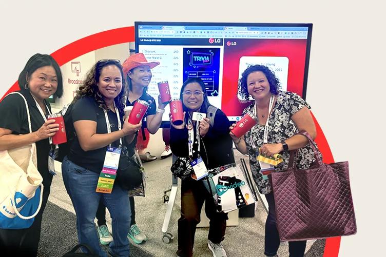 A group of LG event attendees smile in front of an LG CreateBoard.