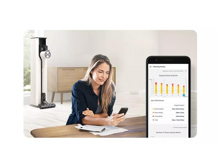 Woman using LG ThinQ app with LG CordZeroTM A9 Vacuum in background