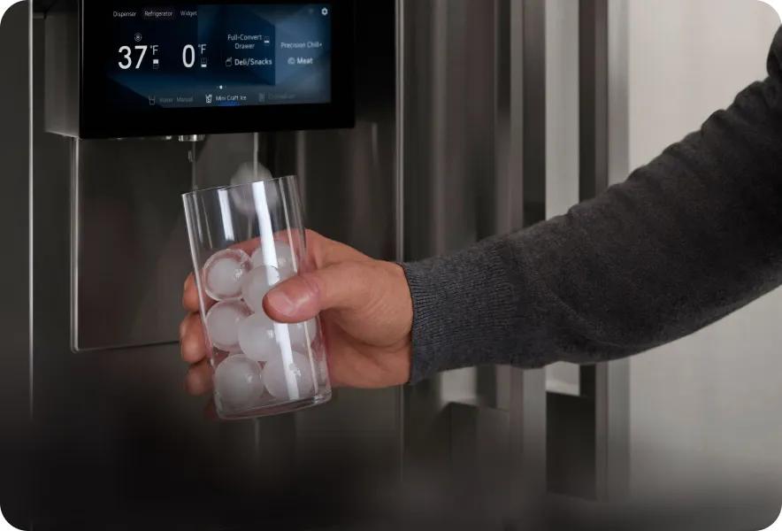 LG SIGNATURE Iconic Collection refrigerator Dual Ice Maker dispensing Craft Ice and into glass from door dispenser with large LDC touch display above.