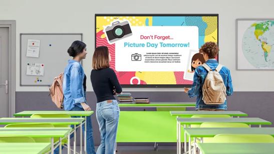 Students look at a notice for school picture day on a CreateBoard in a classroom