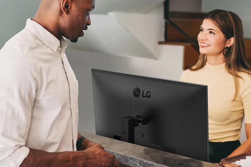 Two people talking over a counter with an LG monitor between them.