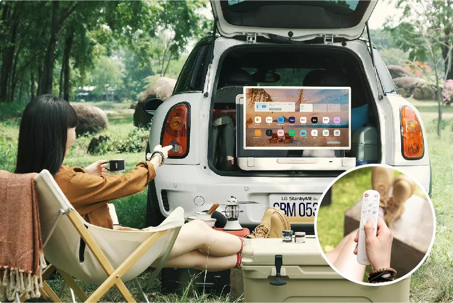 People sitting in camping chairs watch TV from the trunk of a parked car. 