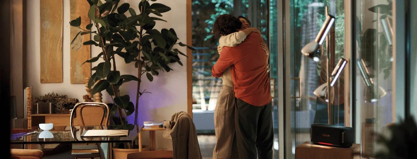 A woman and a man embrace in the living room, with the XBOOM speaker turned on beside them.