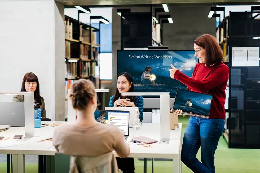 A librarian works with teens using LG grams in a school library. An LG display is behind them.