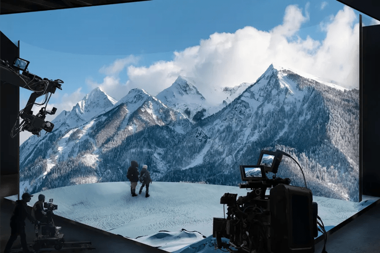 A darkened film studio, with cameras pointed at two actors. LG Studio Series DVLED makes up the set, showing snowy ground and mountains.