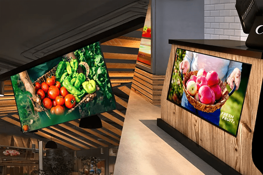 Two digital screens displaying baskets of fresh produce: tomatoes and peppers on the left, apples on the right.