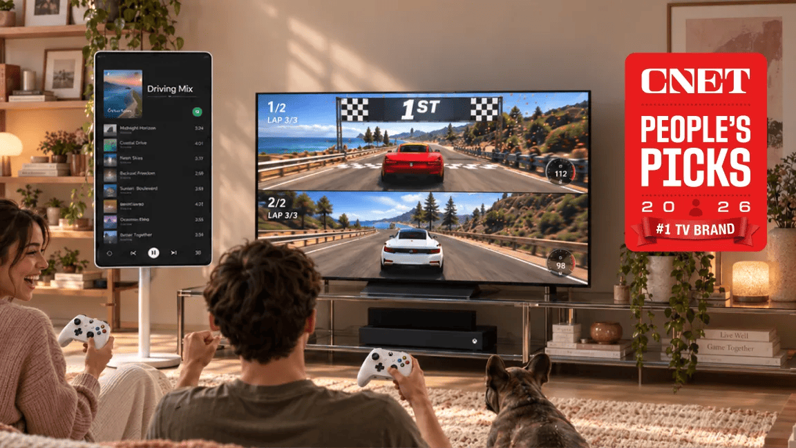 Two people and a dog in a living room playing a split-screen racing game on a large LG TV with Xbox controllers, featuring a vertical smart display to the side and a CNET People's Picks 2026 #1 TV Brand badge.
