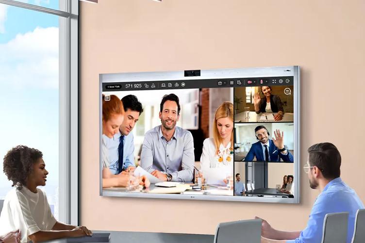 A group of professionals sitting in a meeting room, looking at an LG One:Quick Works displaying a video conference call.